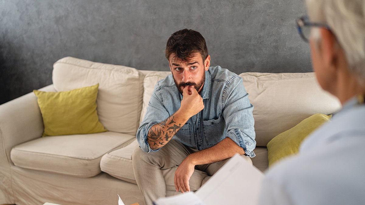 Concerned adult patient sitting on a couch talking with a doctor Concerned adult patient sitting on a couch talking with a doctor