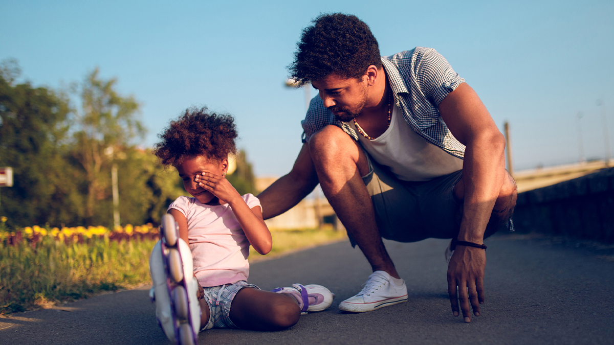 — title missing — A father is comforting his daughter who just fell rollerblading