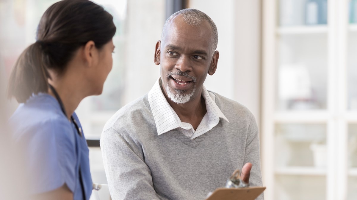 A female healthcare provider talks to a male patient in an office.