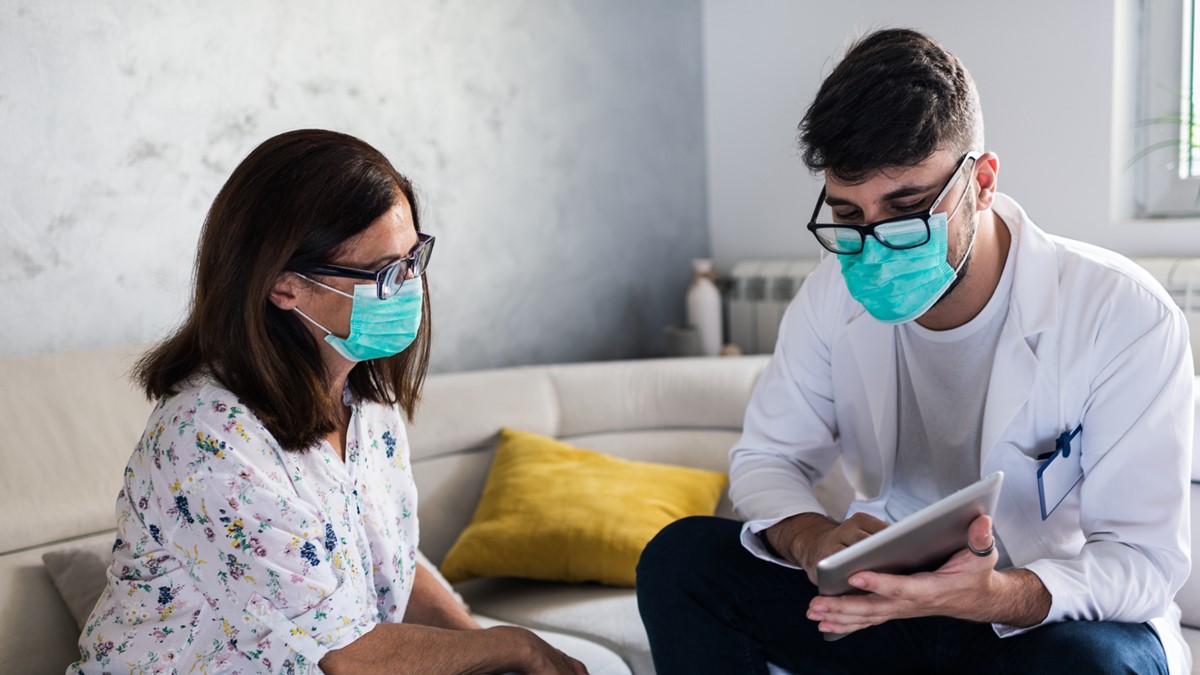 A healthcare provider sits near a woman in an office. He has a tablet in his hand to share information.
