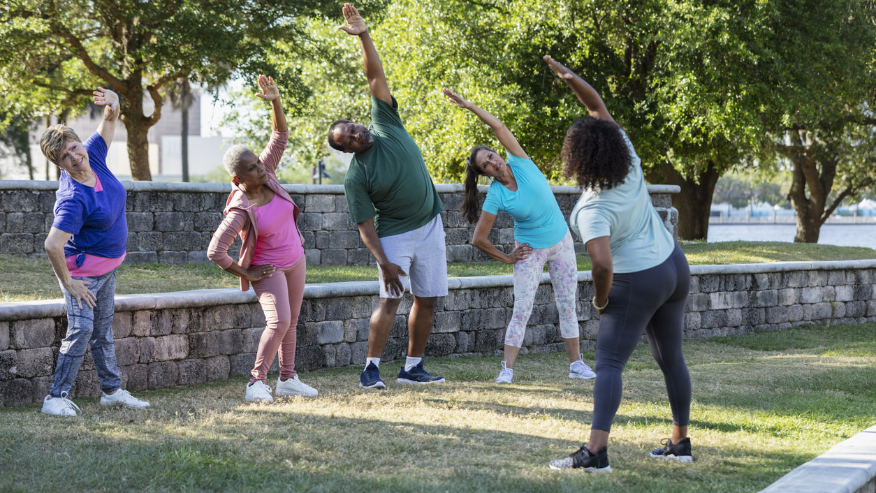 Group exercise class with instructor at park, stretching People stretching in the park as a group