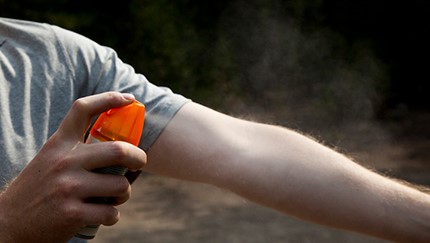 A man spraying bug spray on his arm.
