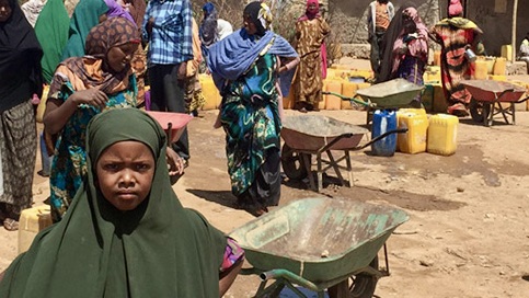 Little girl from a village standing beside a wheelbarrow