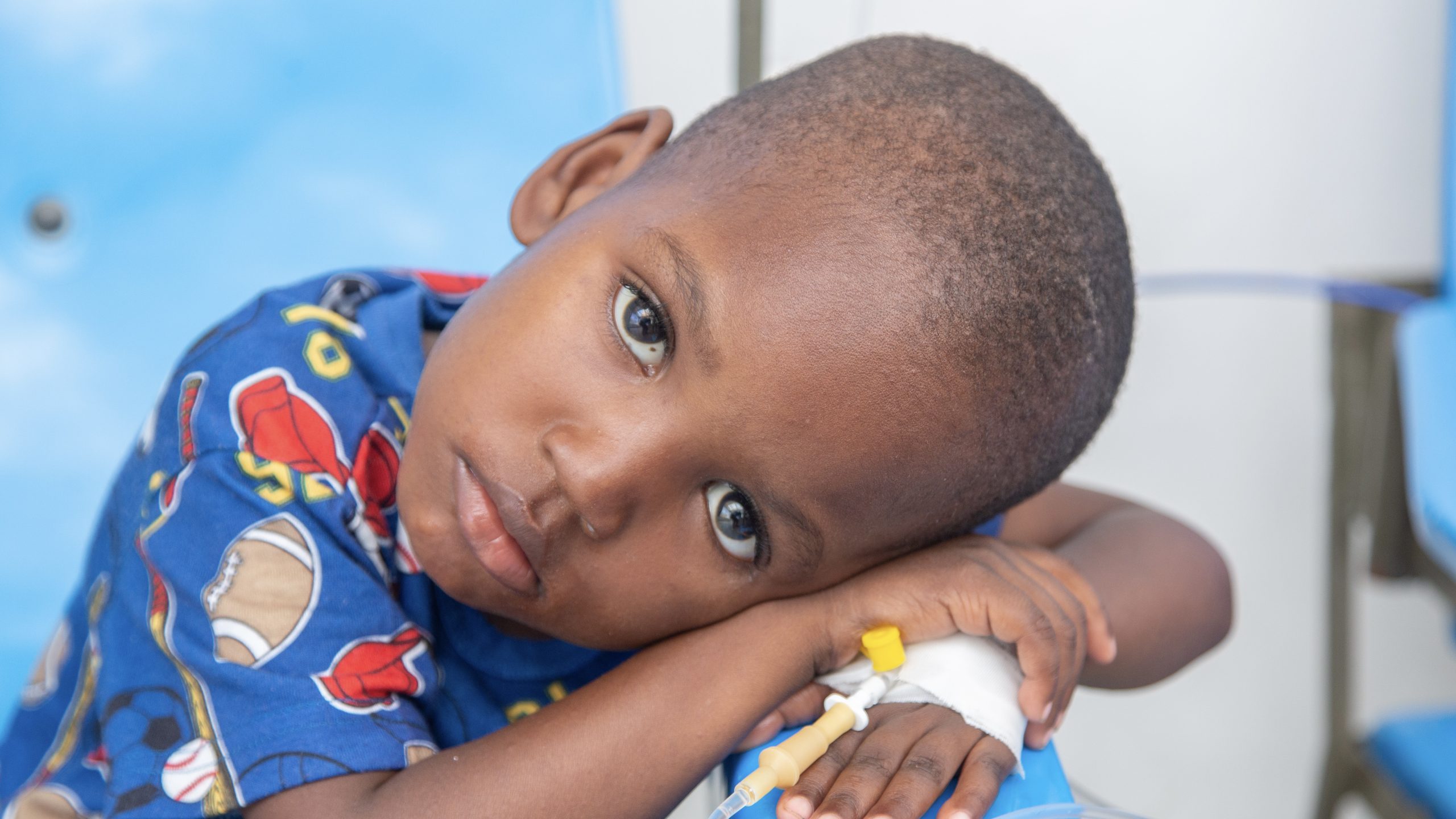 Young boy with his head resting on his crossed arms with IV in his hand
