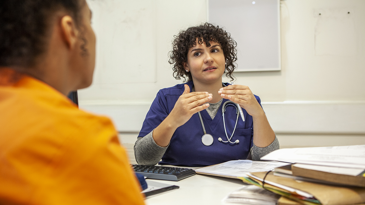 Correctional Health Doctor Gives Consultation to Incarcerated Person A female correctional health doctor provides a consultation to a female incarcerated patient.