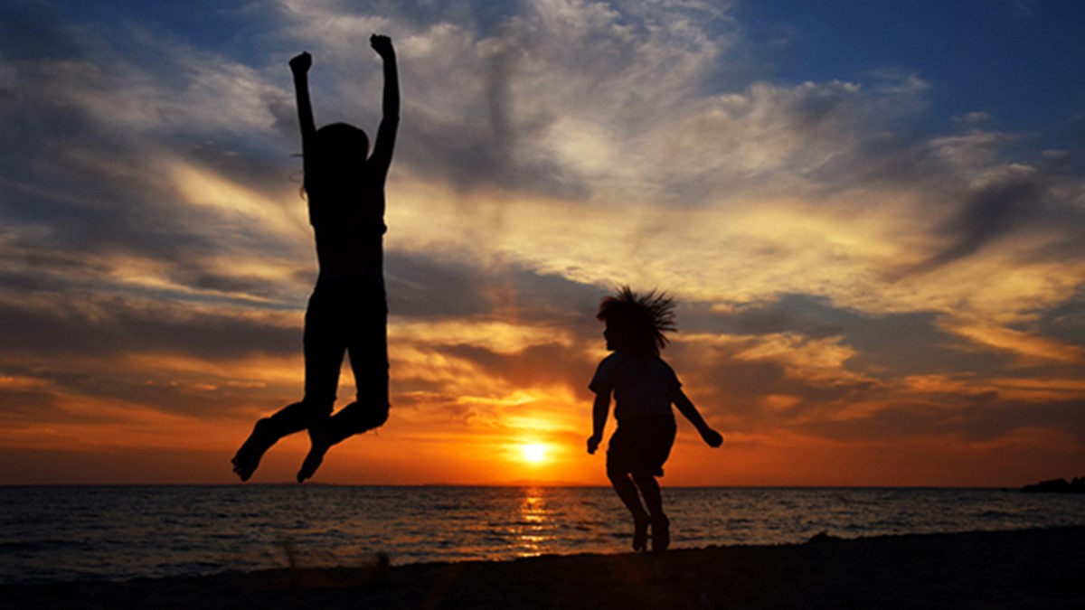 Happy young family have fun on beach and jump at sunset