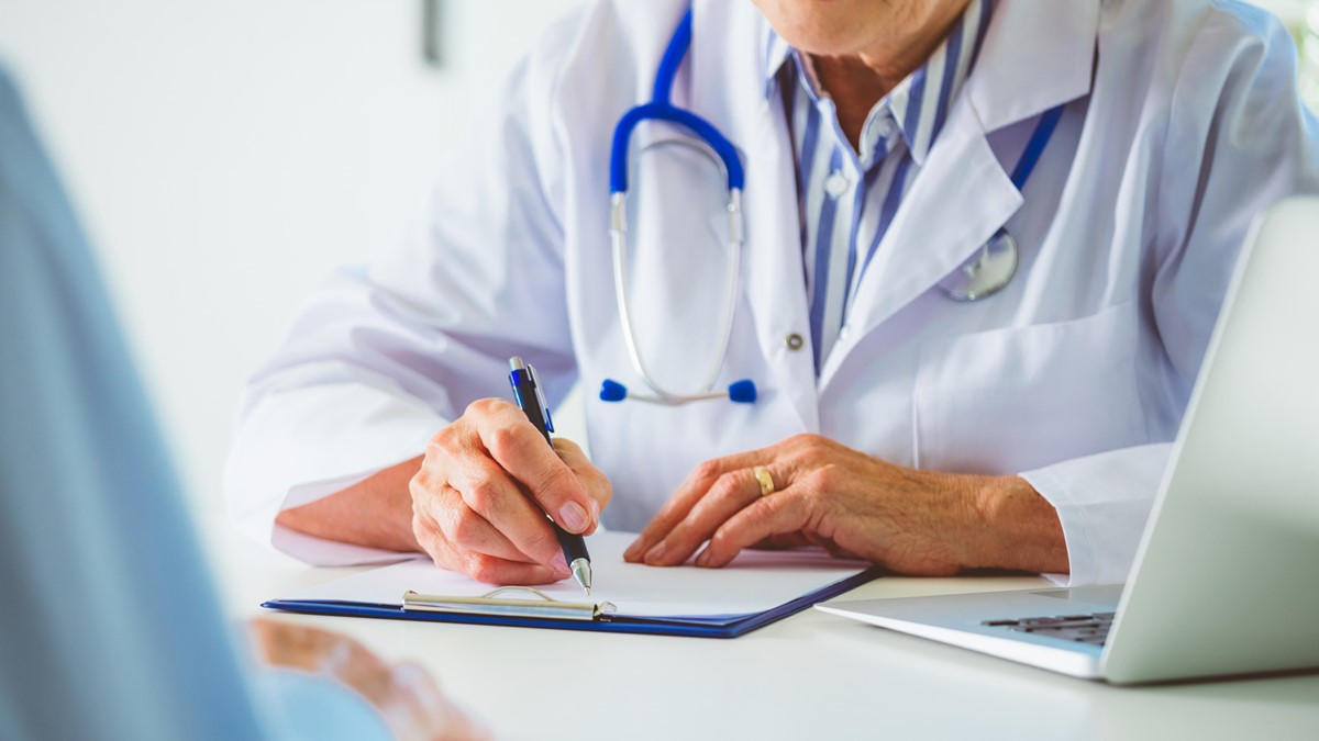 A healthcare provider writing on a clipboard across the desk from patient.