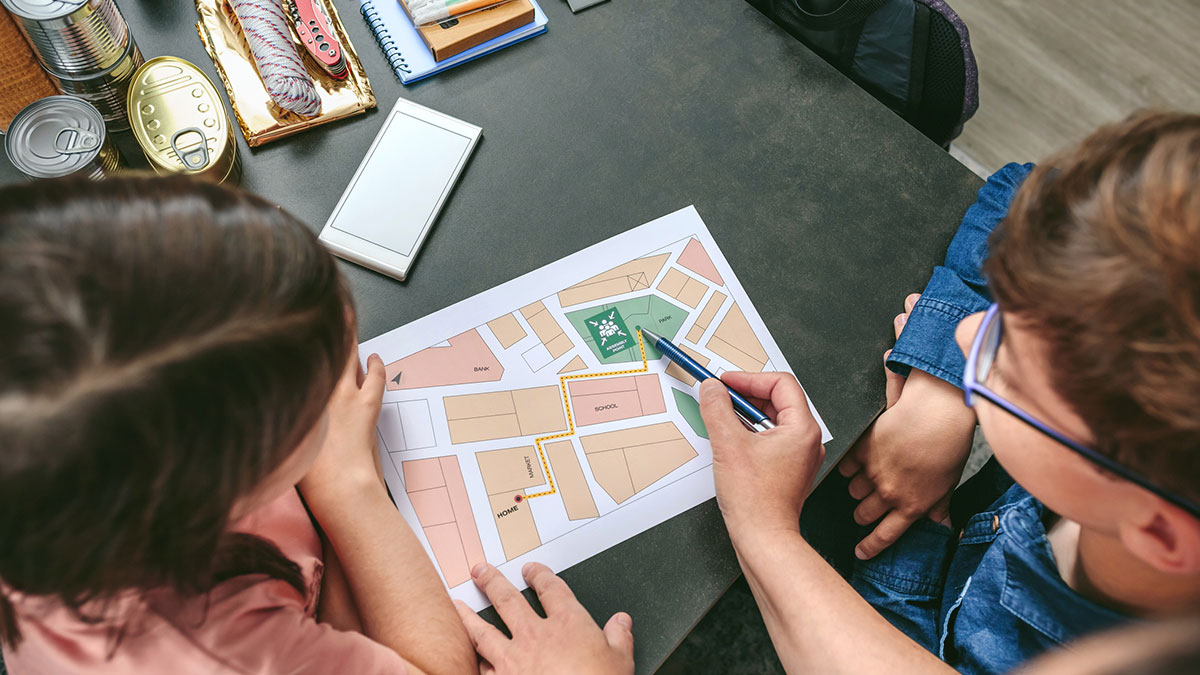 Mother explaining evacuation route to children Top view of unrecognizable mother explaining to her children the assembly point map while preparing emergency backpacks