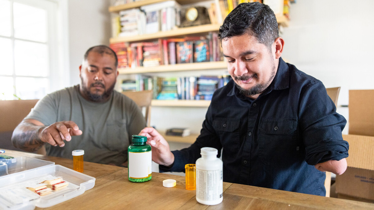 Man with disability gathering medicine Two veteran disabled hispanic housemates packing a disaster response kit