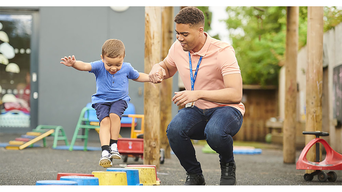 Caregiver helping boy jump An early educator helping a child jump on the playground.