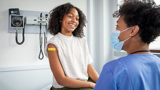 Healthcare professionals A healthcare provider wearing a mask and chats with a smiling patient with a bandage on their upper arm.