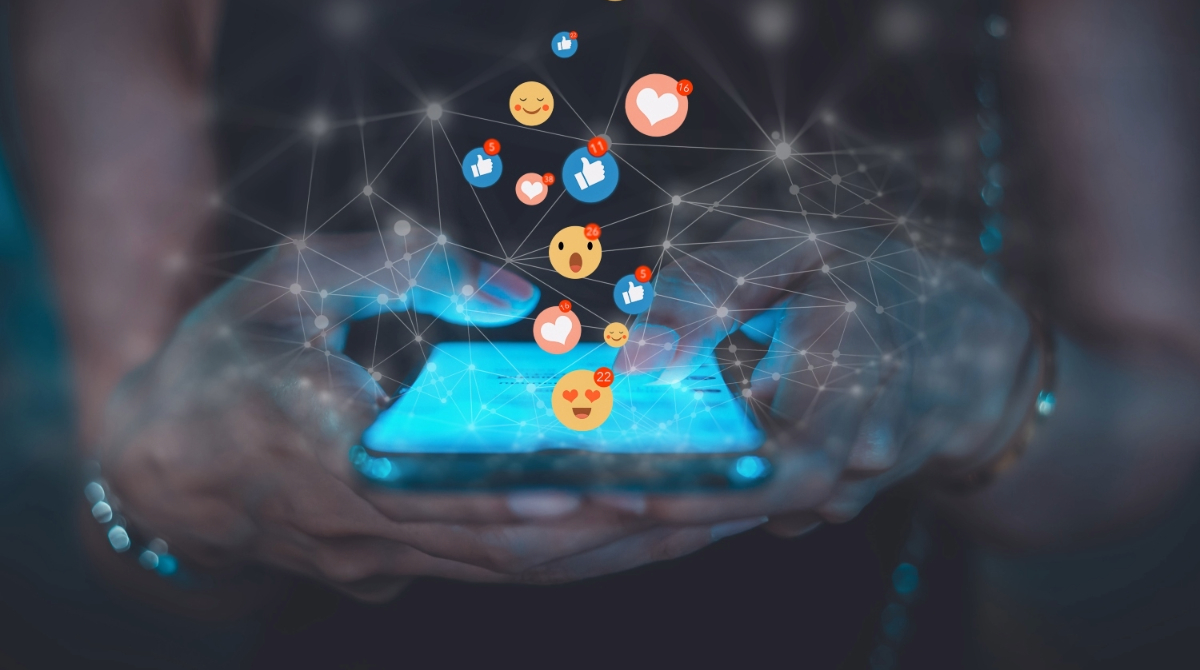SocialMediaBanner_Graphic Close up of a person using smartphone with social media emojis floating above the phone screen.