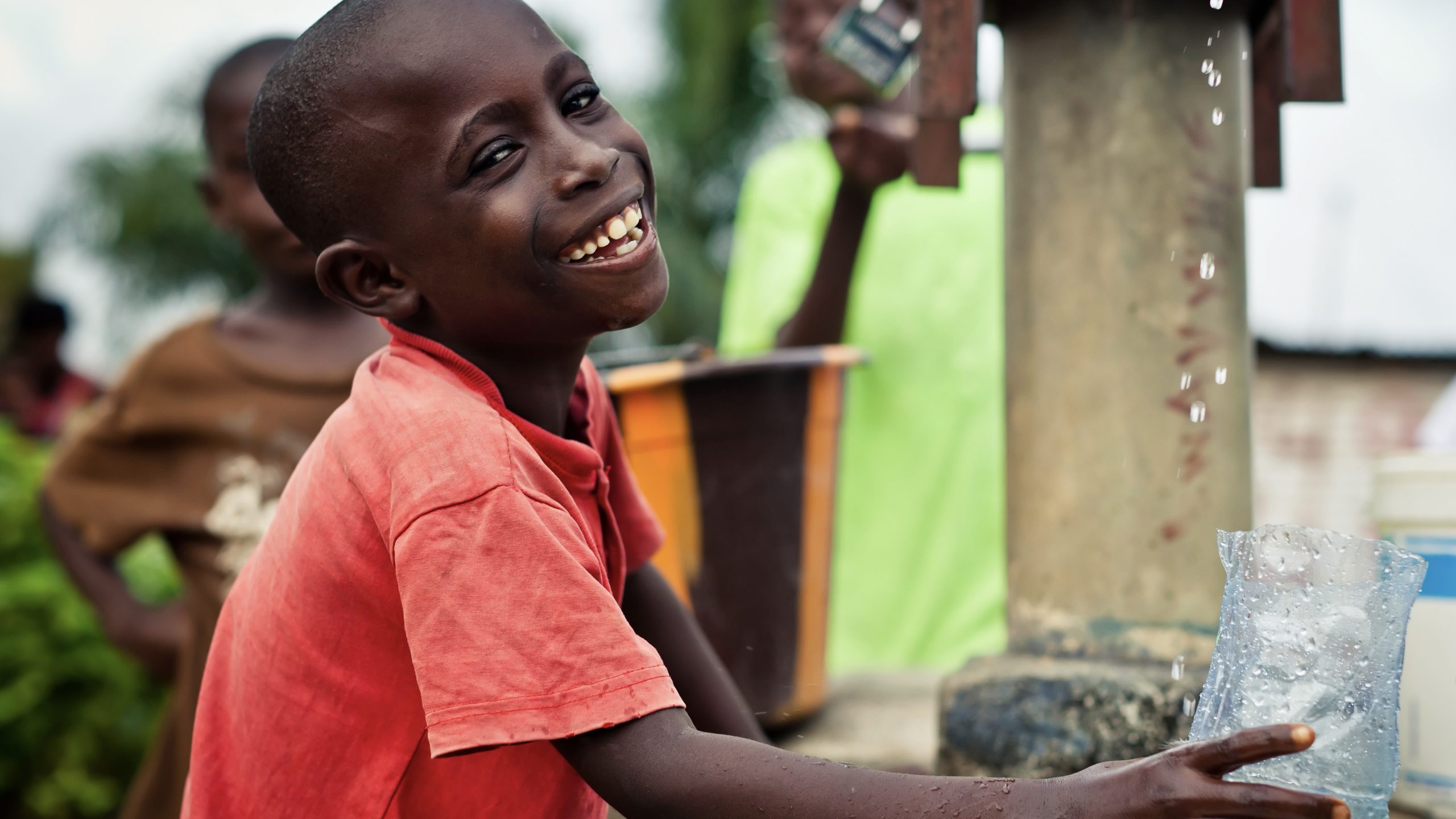 Smiling boy holding glass getting water from a pump