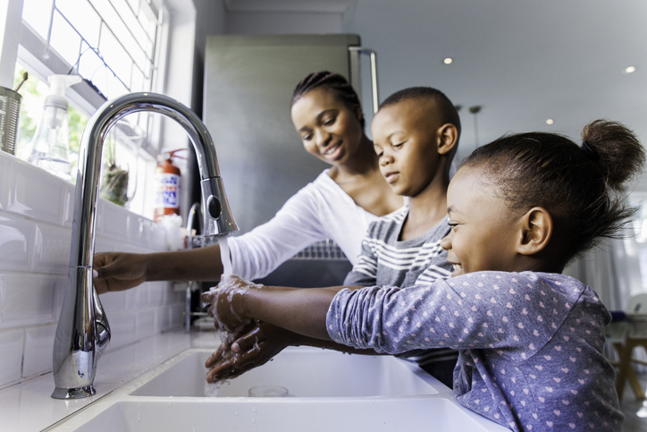 Family washing their hands together. Family washing their hands together as the mom supervises her children.