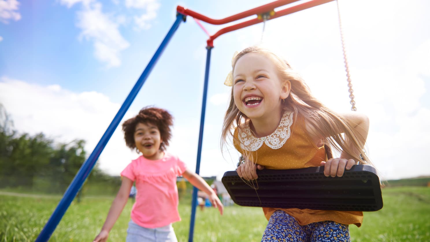 The best friends playing together Child on a swing with another child approaching the swings.