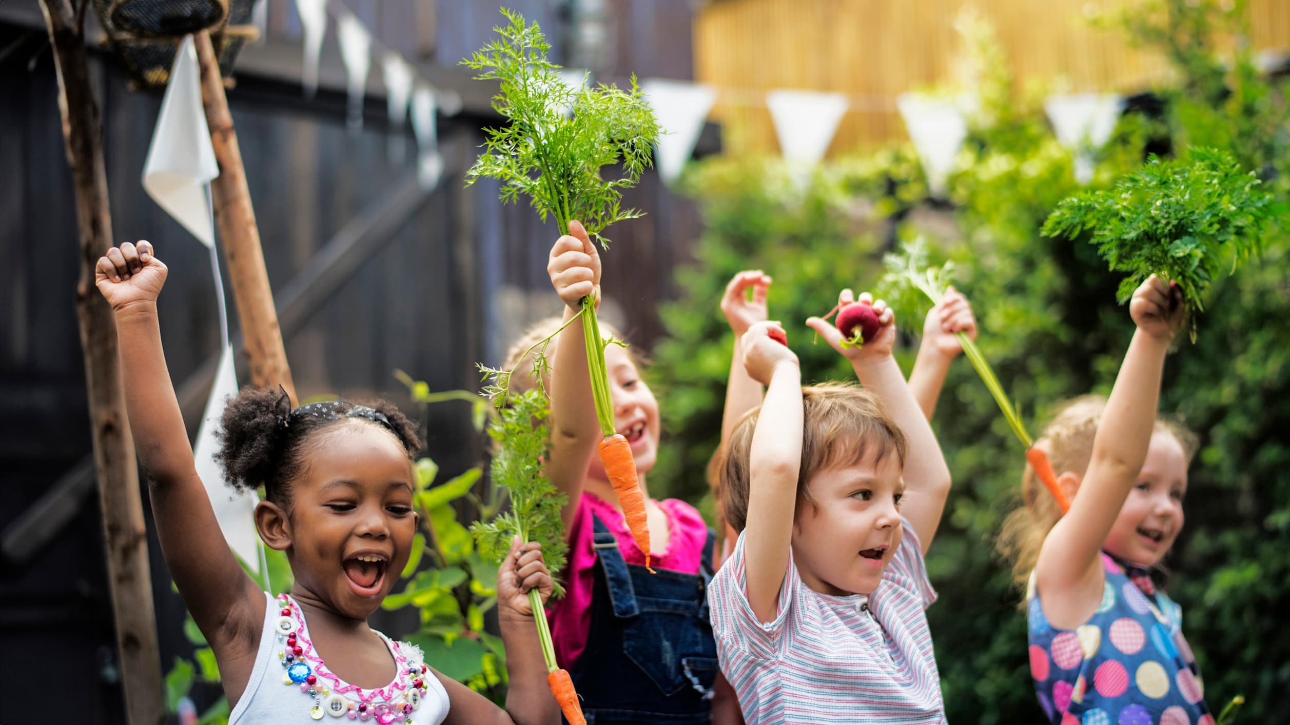 Kids in a vegetable garden with carrot Children in a garden, with their hands up in the air, holding picked greens.