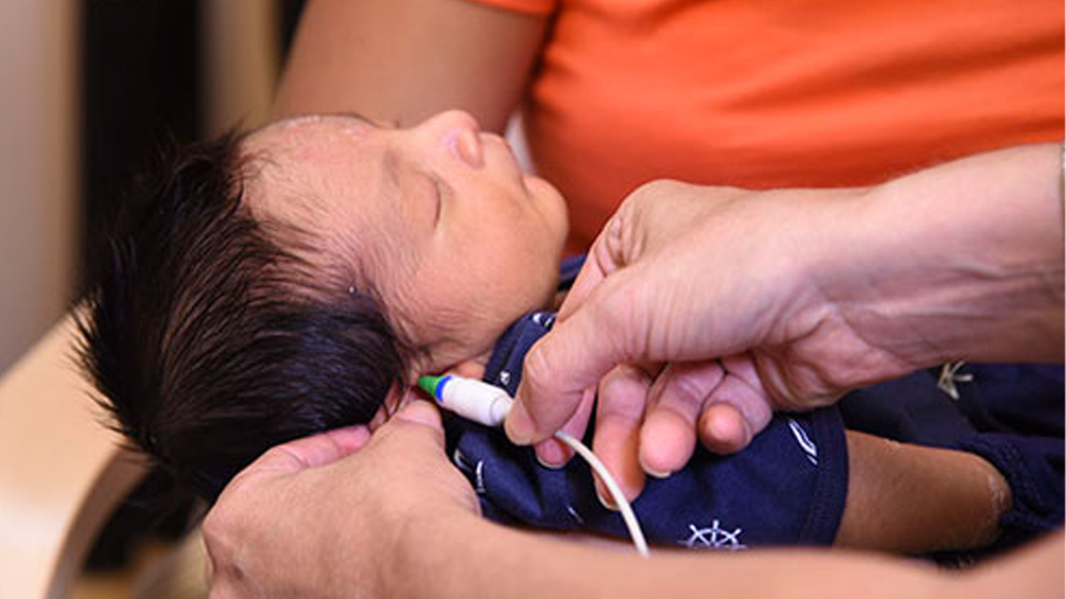 baby getting hearing checked at the office Newborn infant with dark hair is asleep while getting a hearing screen