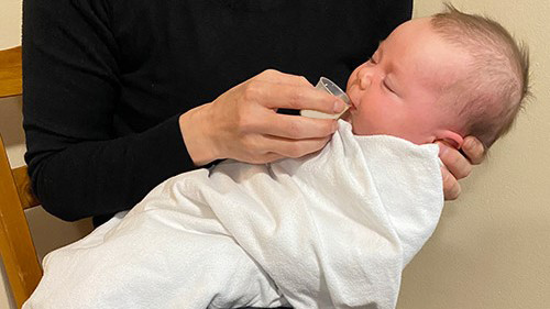 Caregiver cup feeding breast milk to a baby. Caregiver cup feeding breast milk to a baby.