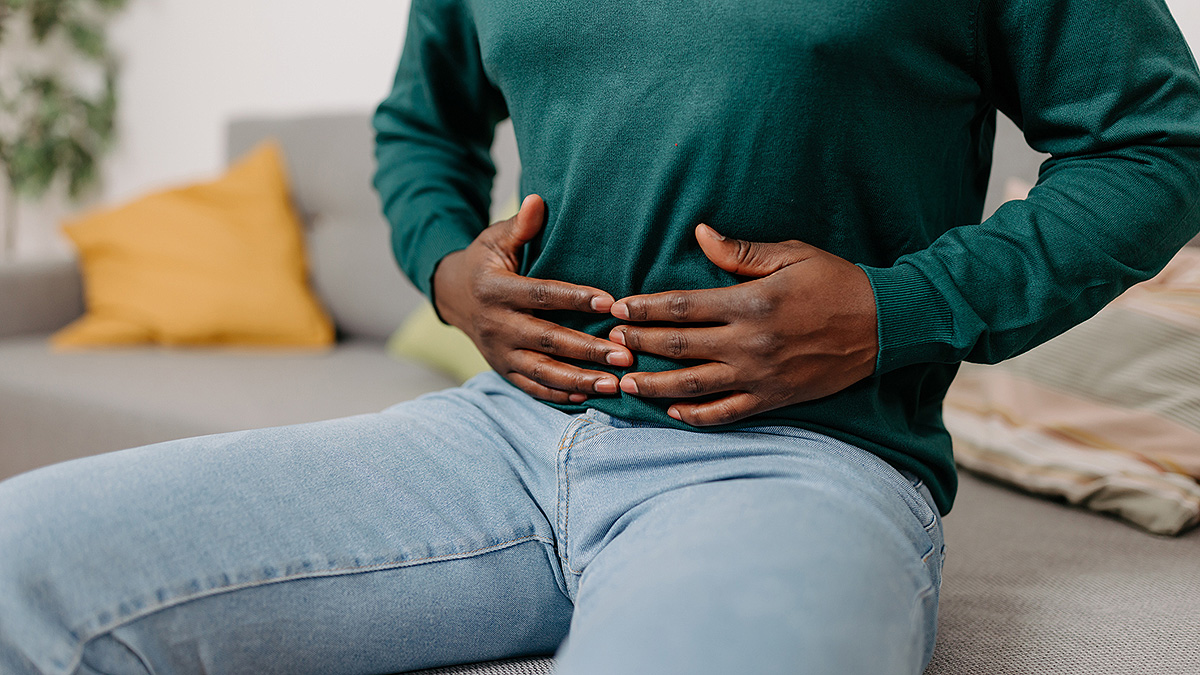 IBD Man With Stomach Pain A young man sits on a sofa, holding his stomach from digestive pain.