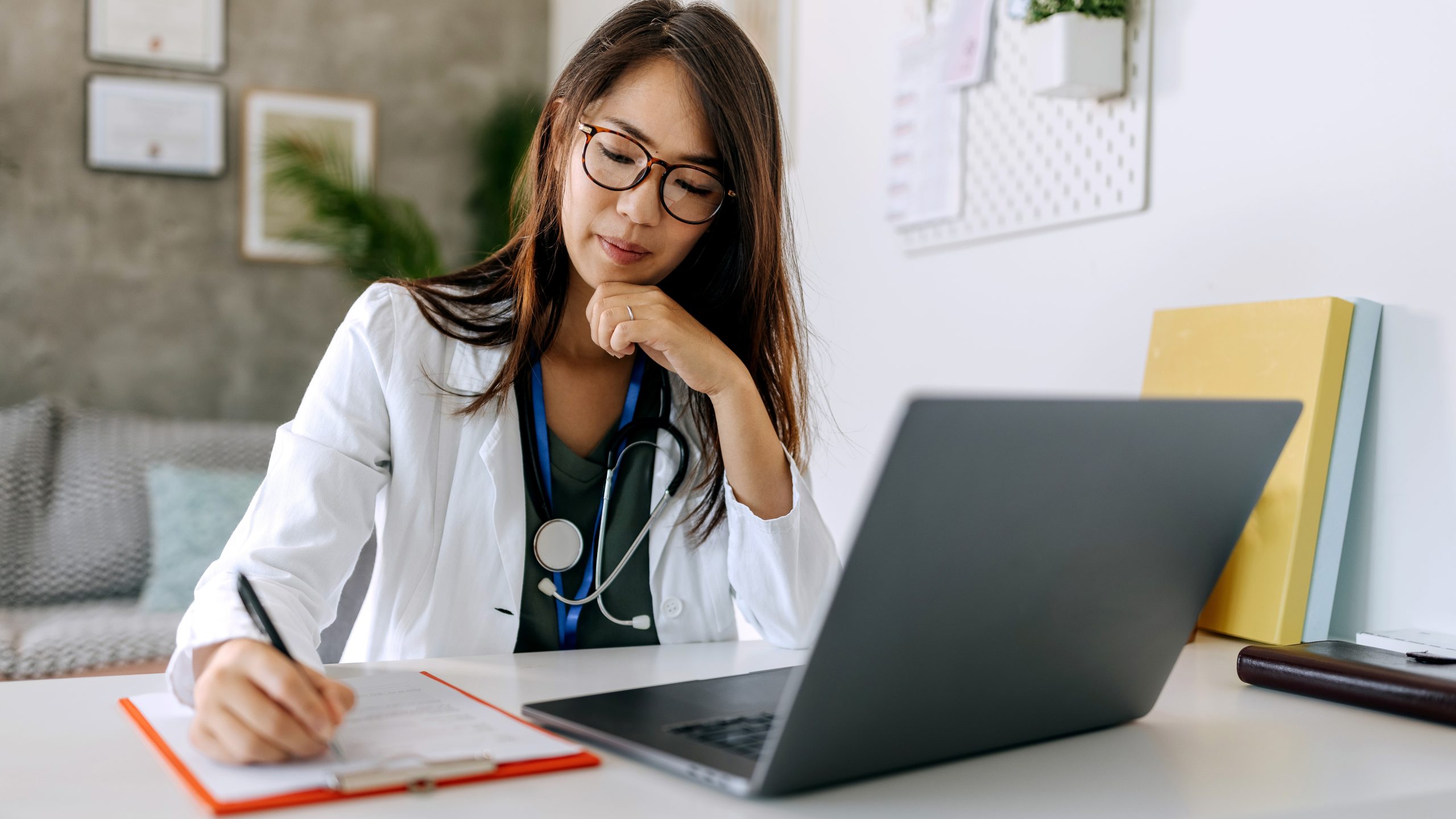 Doctor on computer Healthcare provider takes note on a clipboard next to a laptop.
