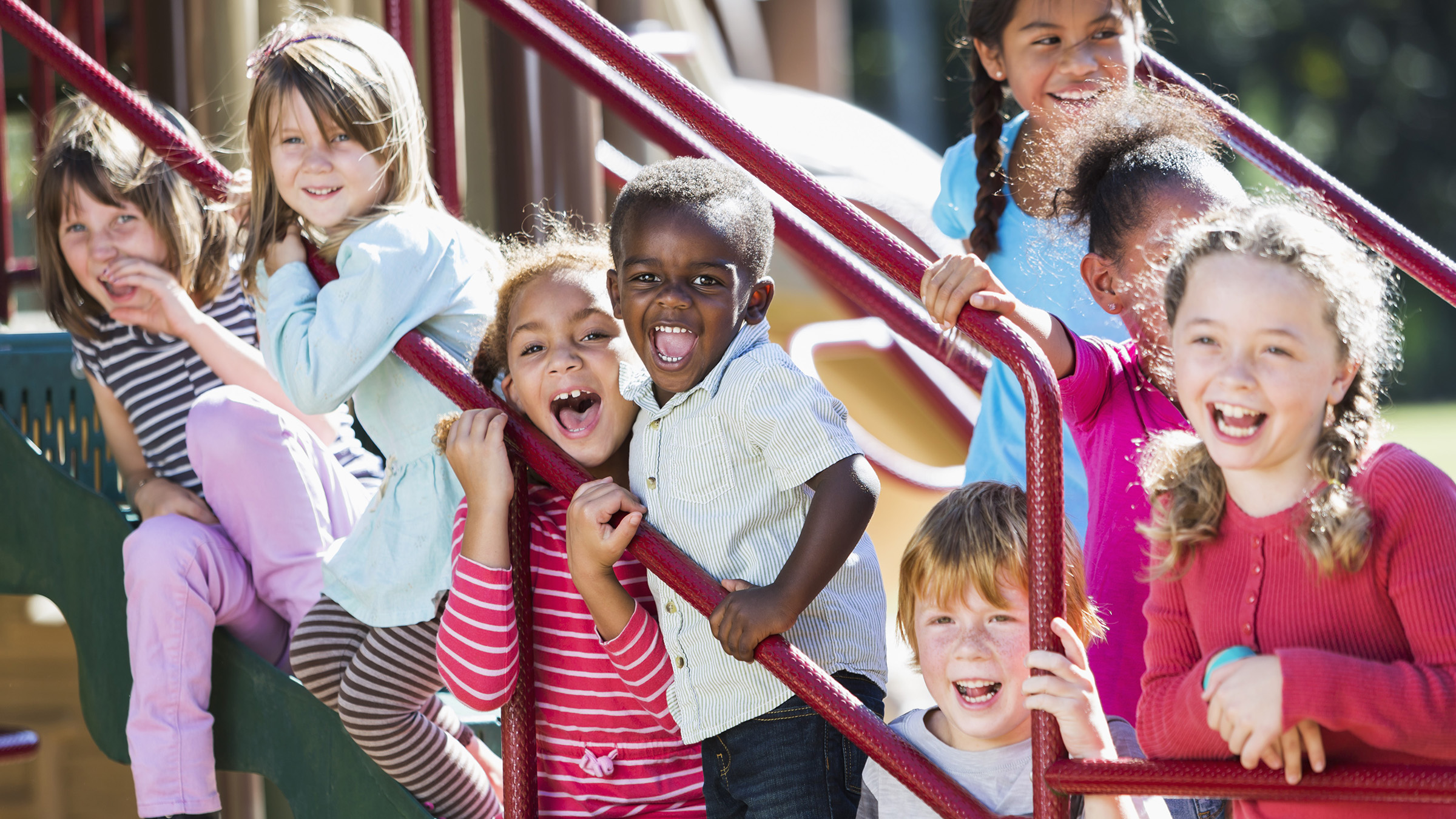 Smiling kids on a staircase outside A diverse group of young boys and girls on playground equipment.