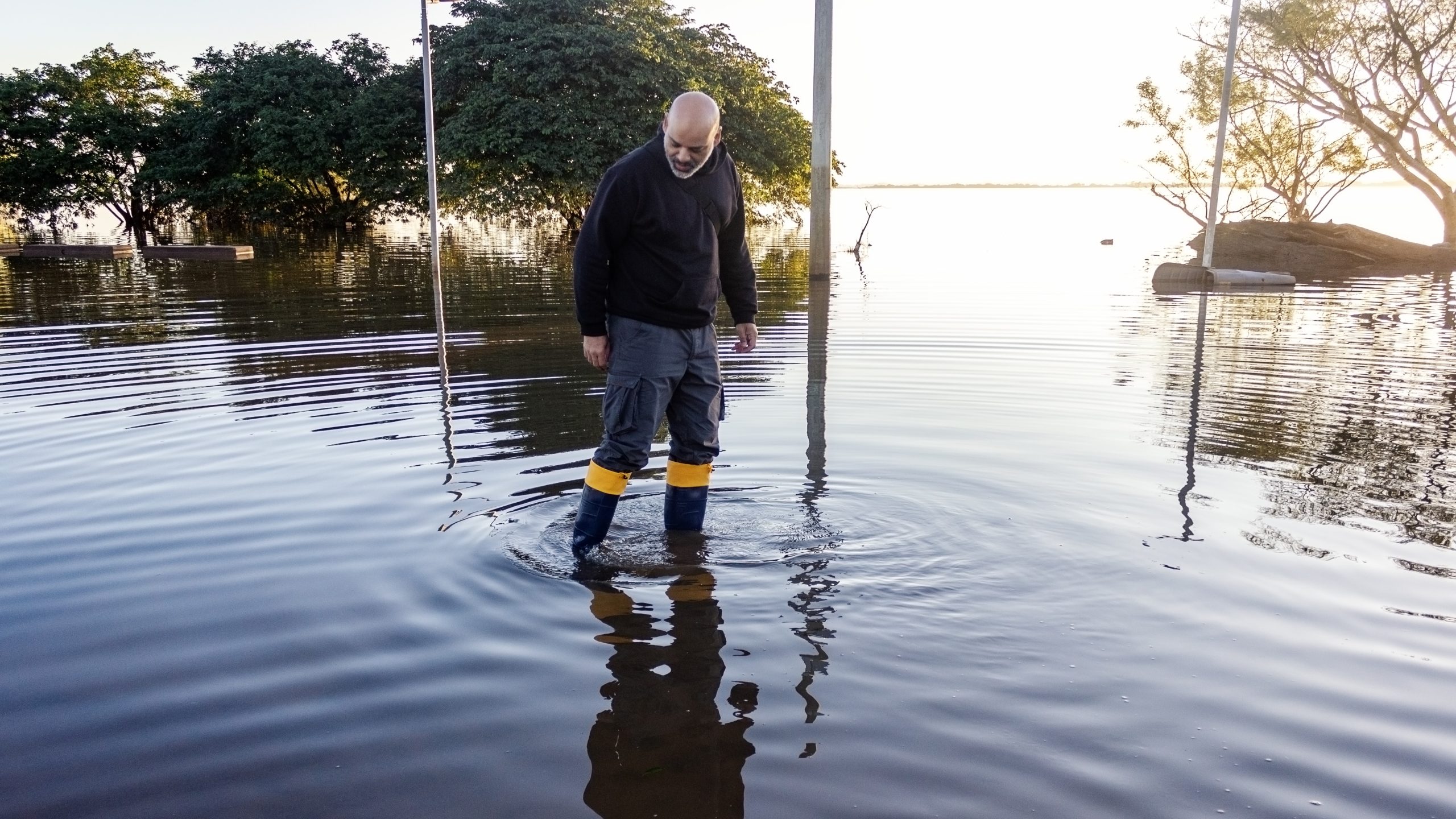 A man in boots walks through a flooded area.