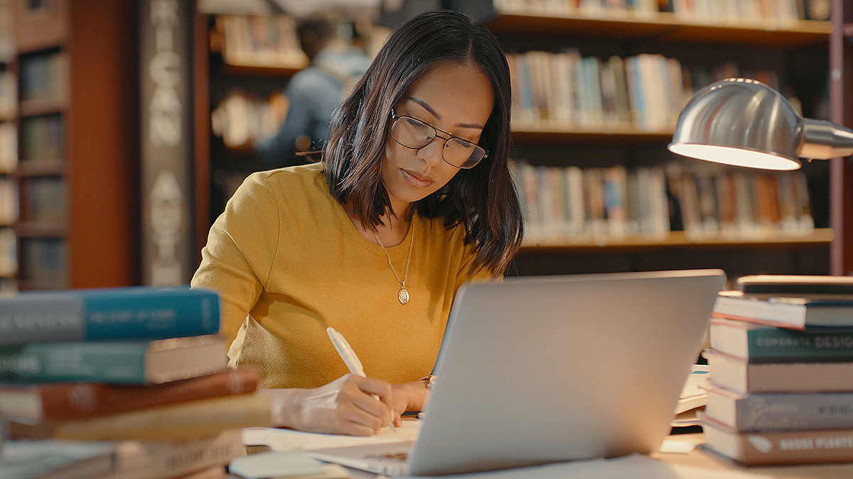 Lupus Research Dark-haired woman in a library with laptop doing research.