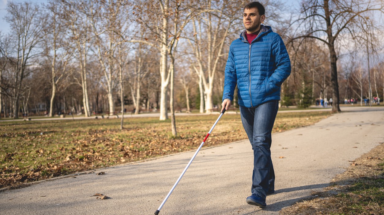 Man walks using a walking cane.