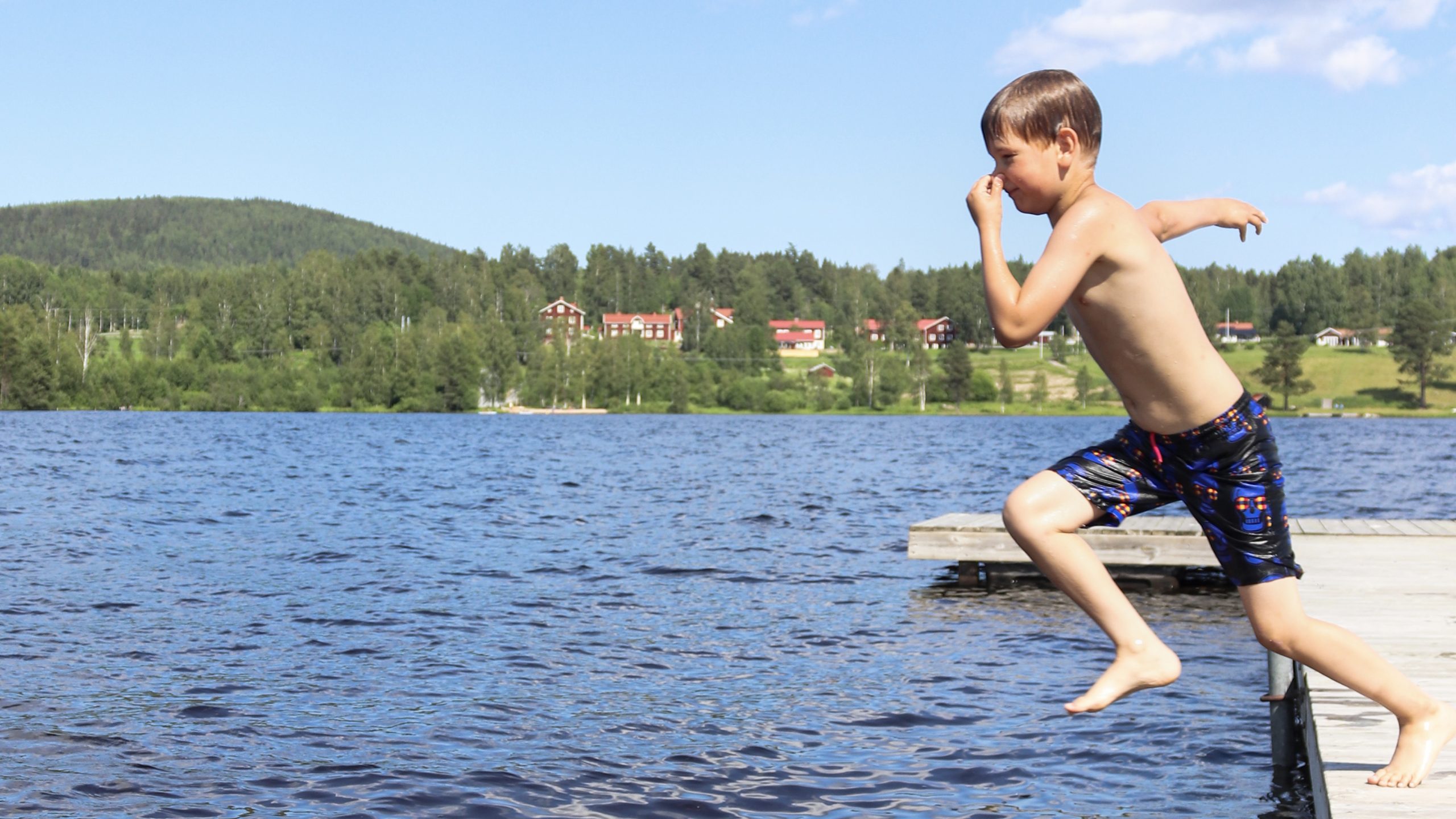 Young boy holds his nose while jumping off a dock into a lake