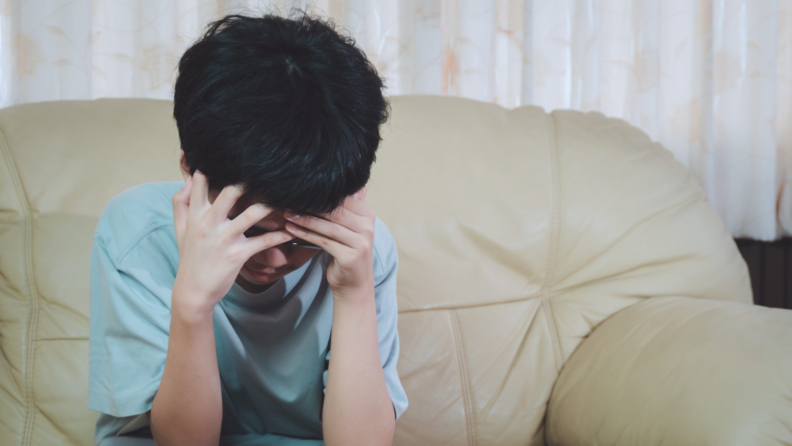 A young boy with his head in his hands seated on a couch.