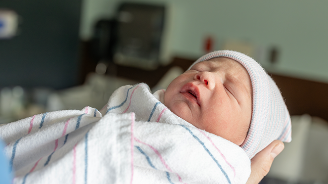 Newborn wearing hat and wrapped in blanket, being held by parent. U.S. births increased 1% from 2023 to 2024.
