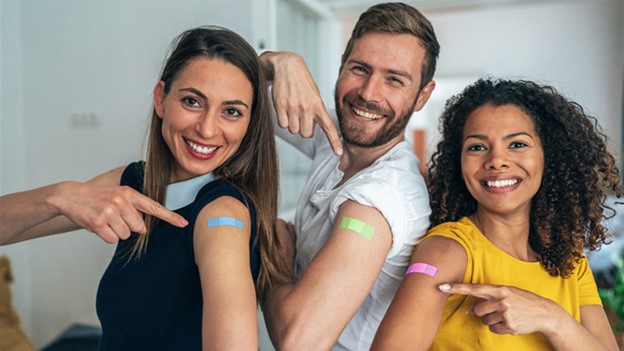 multicolor band-aids Three people smile and point to their upper arms, showing their colored band-aids.