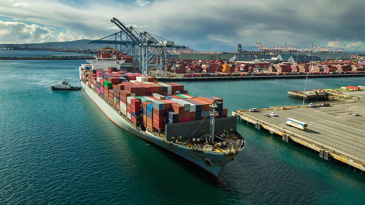 NIOSH Maritime Center Aerial image of a cargo ship loaded with containers with a row of cargo cranes in the background.
