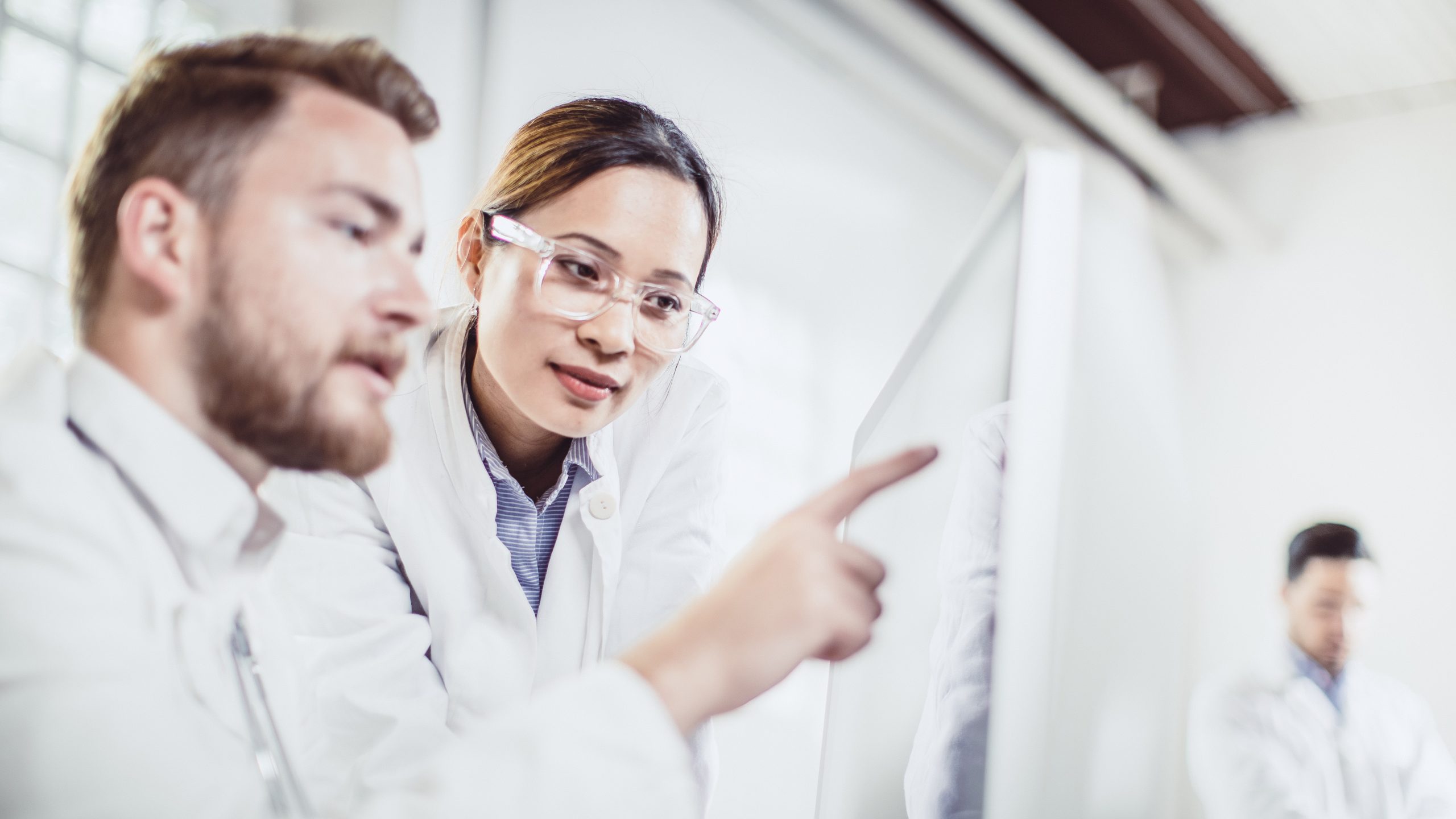 A physician pointing to an x-ray screen with another physician looking at the screen.