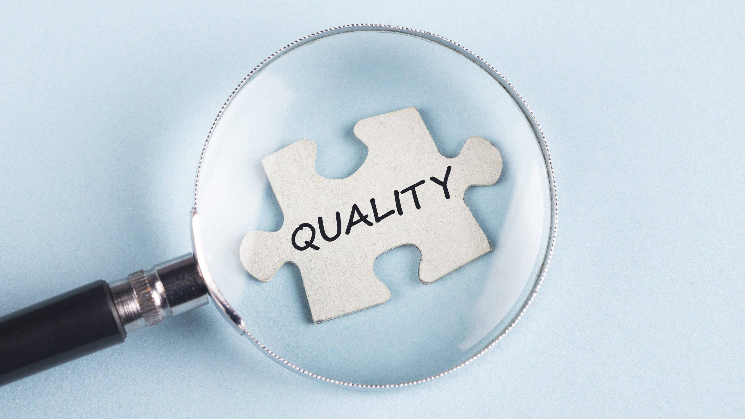 A magnifying glass over a puzzle piece with the word "Quality" on it.