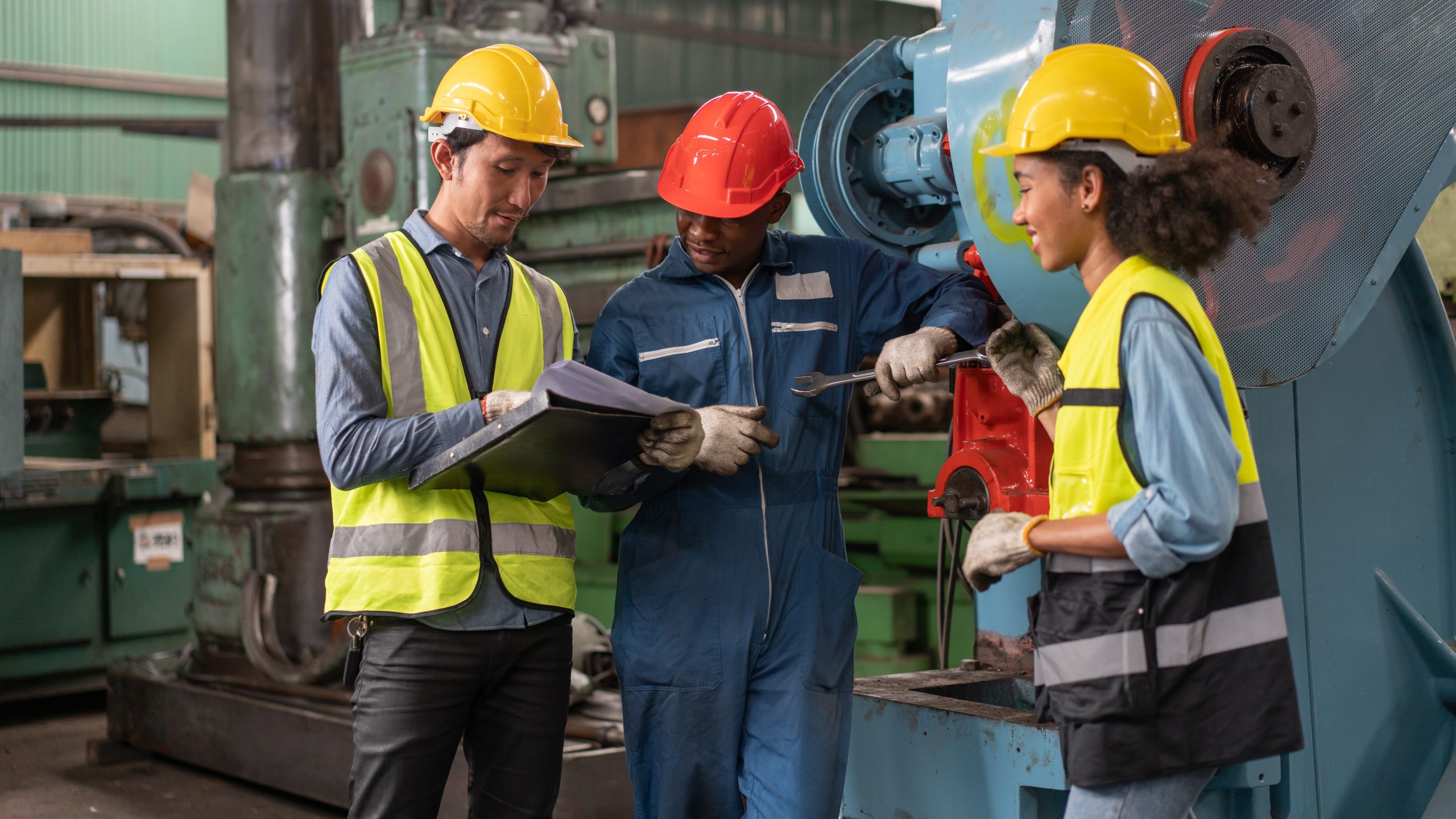 Engineers in safety vest with helmet look at machine specification documents Engineers in safety vest with helmet in front of a factory machine.