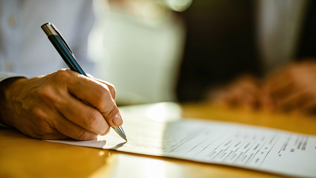 — title missing — a hand holding a pen writing on a white piece of paper on top of a wooden tabletop