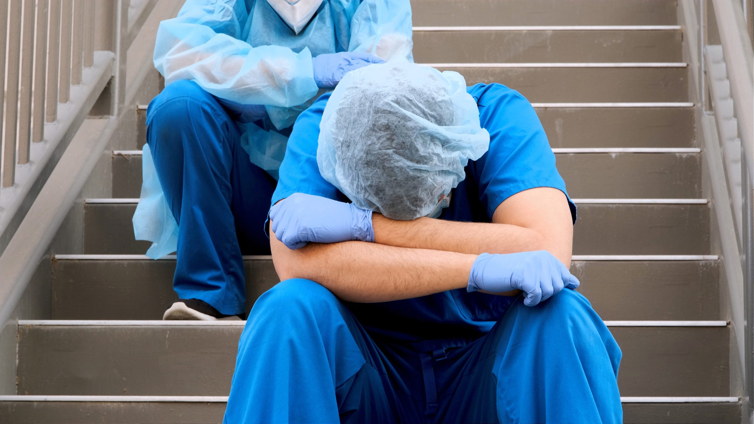 -- title missing -- Two overworked healthcare workers sitting on stairs.