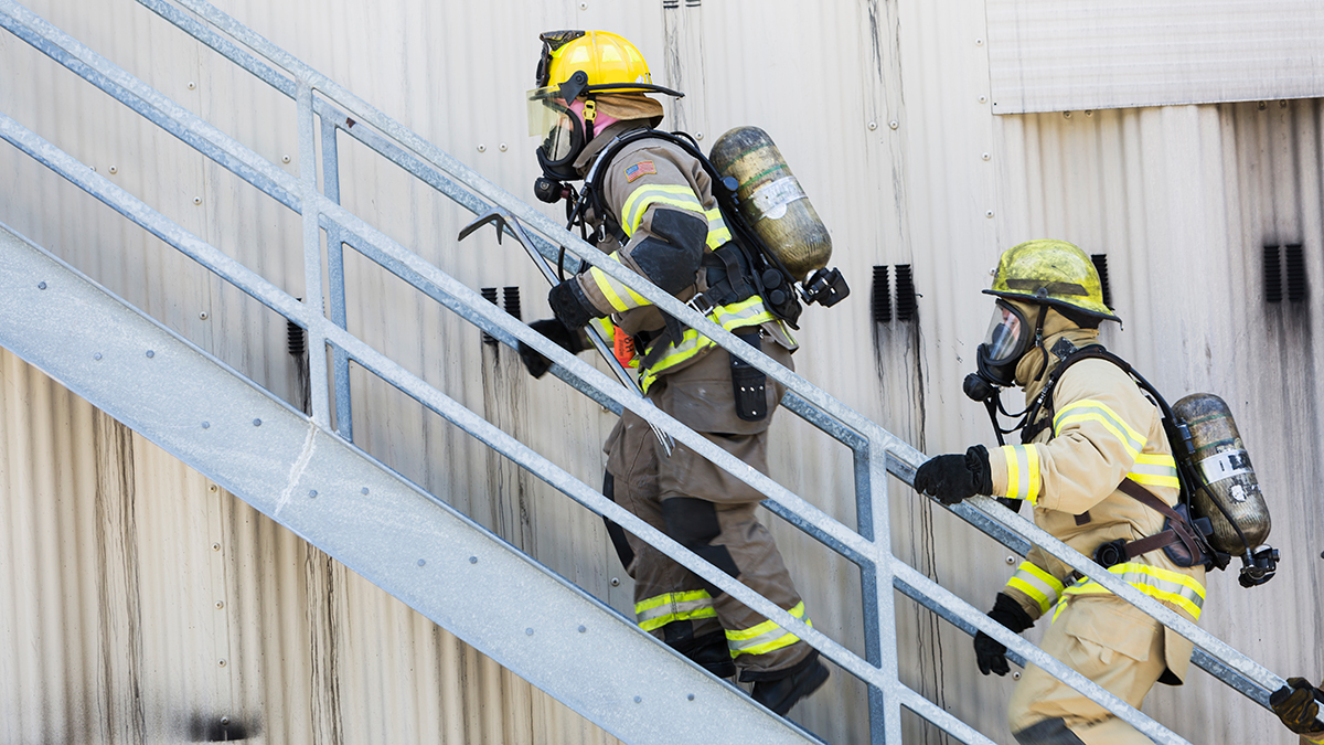 — title missing — Two firefighters in gear climb exterior stairs