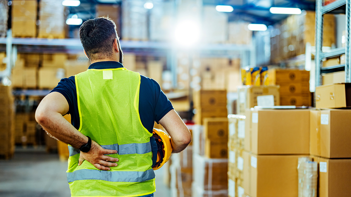 Warehouse worker with back pain Warehouse worker in safety vest holding his lower back