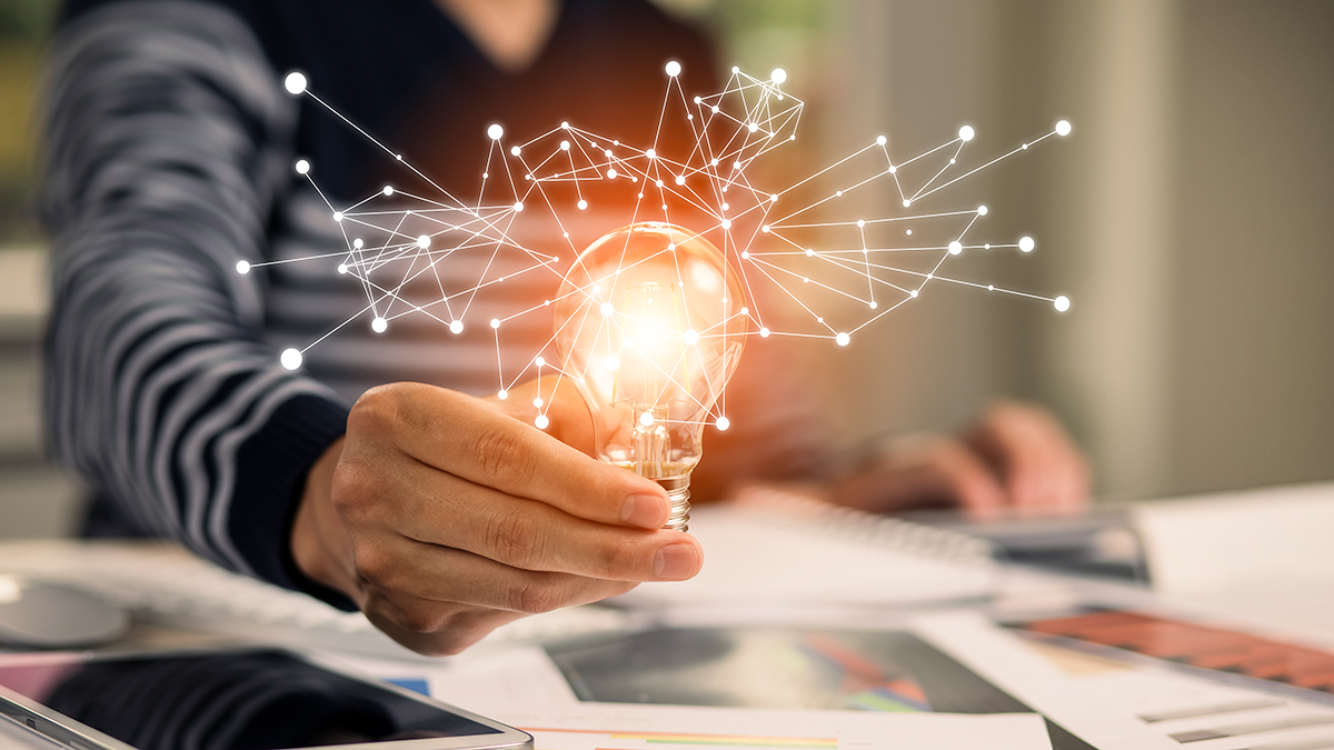 — title missing — Person at desk with papers holding up lightbulb casting light