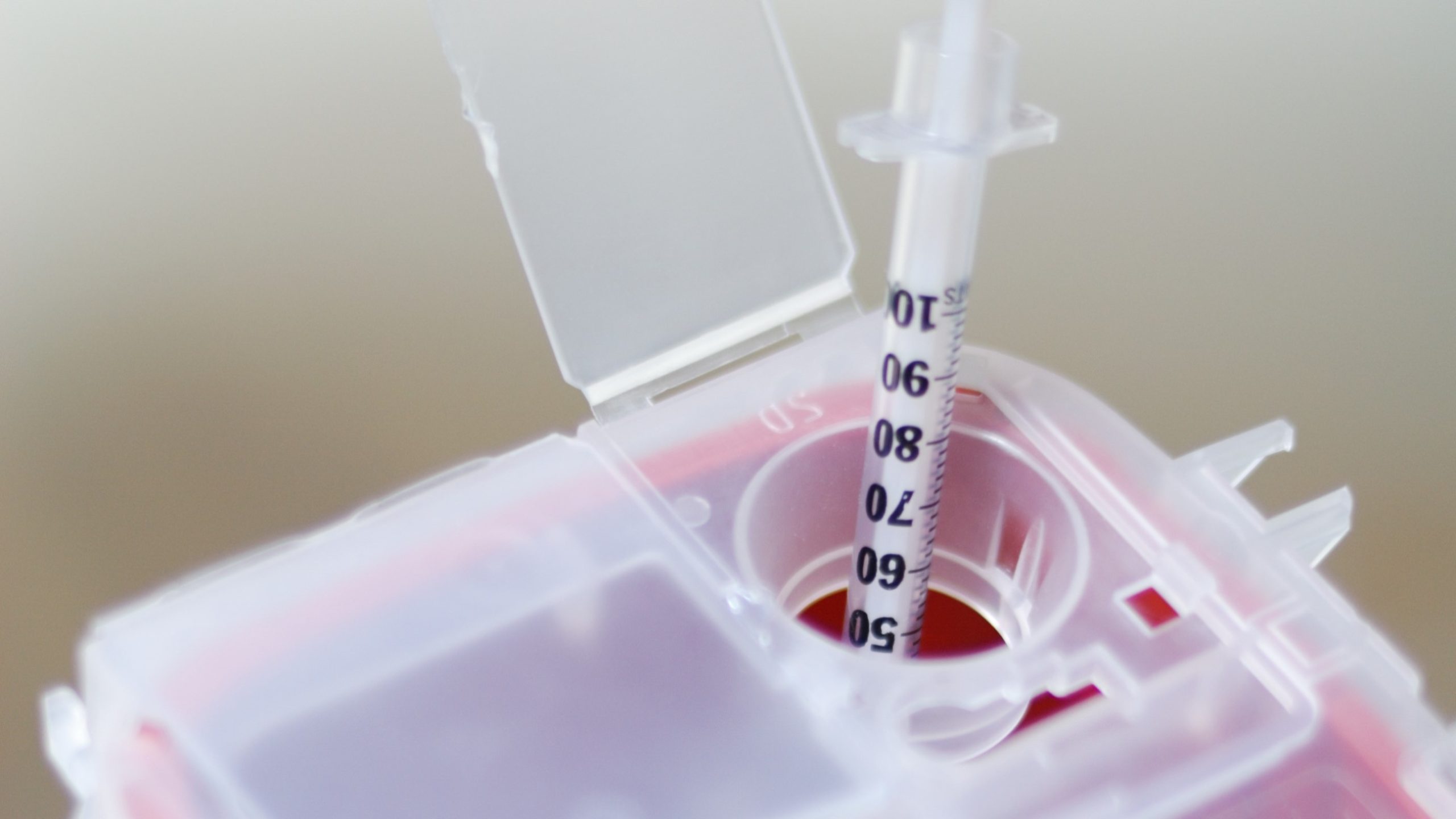 A needle being put into the top of a sharps disposal container.