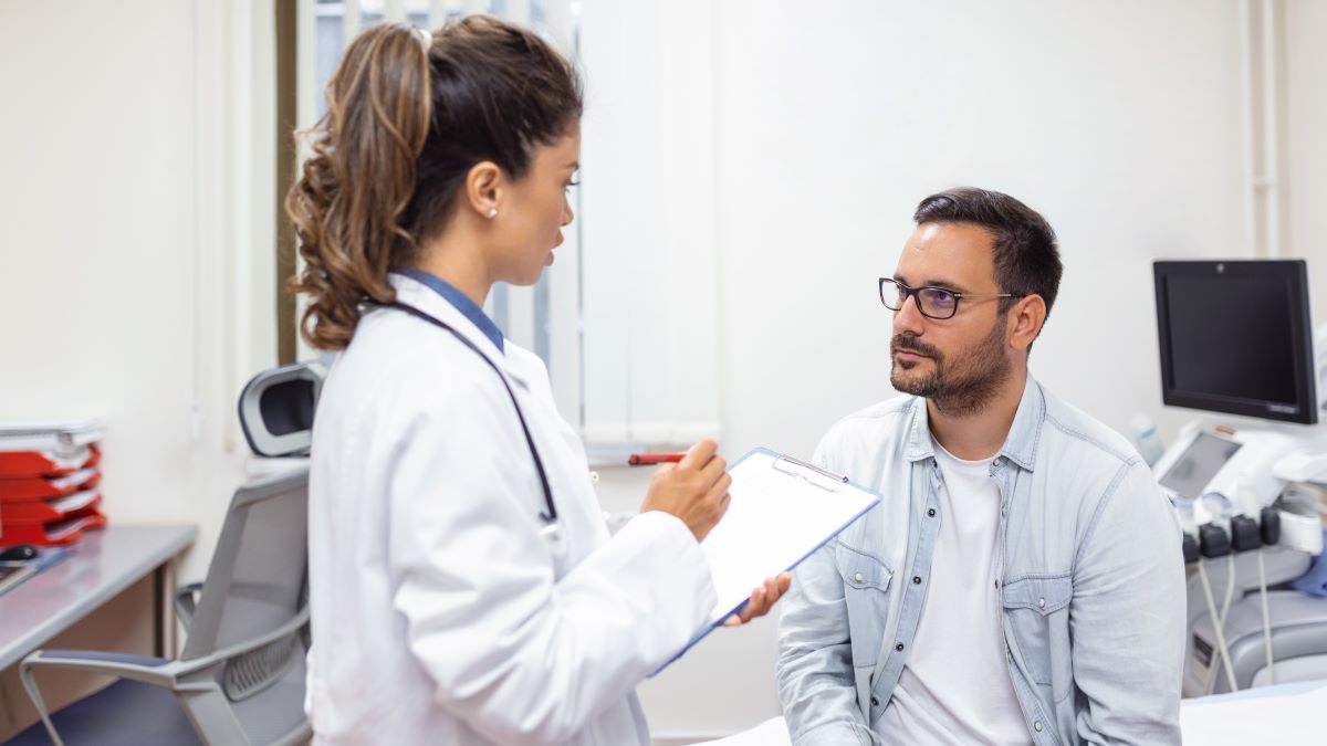 Female doctor and male patient Female doctor stands as she talks to a sitting male patient in exam room.