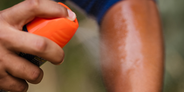 A person sprays insect repellent onto their left arm.