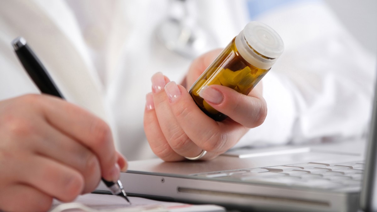 A healthcare provider holds a medicine bottle and writes a note with a pen.