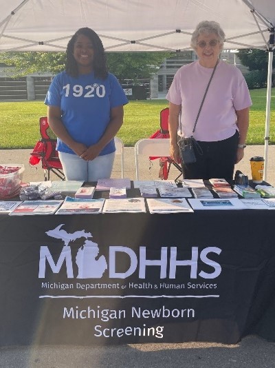 Two people stand behind a MDHHS table with newborn screening resources