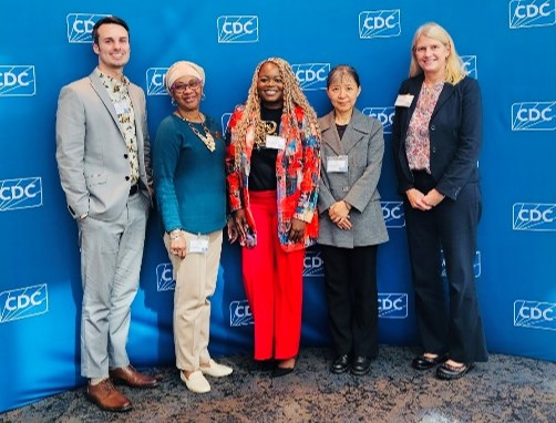 Five persons stand together in front of a CDC logo backdrop