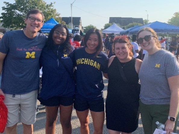Five persons in athleticwear pose together outdoors