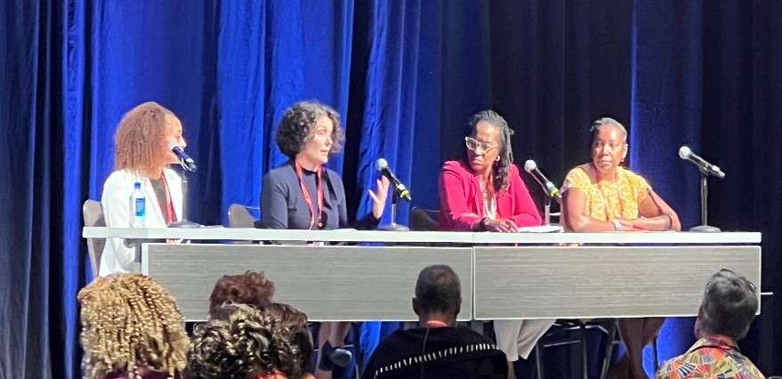 Four persons sit at a table with microphones on a stage