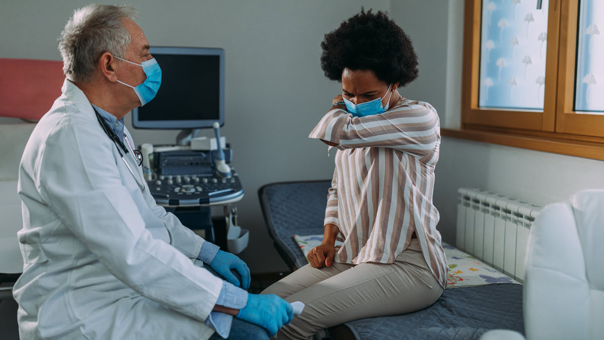 Health care provider with coughing patient A health care provider observes a patient coughing during a medical exam.